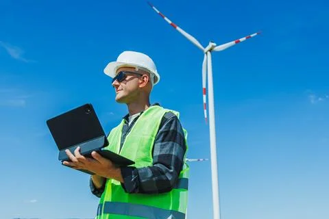Worker checks data on a tablet near a wind turbine in a renewable energy pa.. 스톡 사진