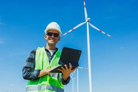 Worker checks data with tablet near wind turbines on a clear day in a renew.. 스톡 사진
