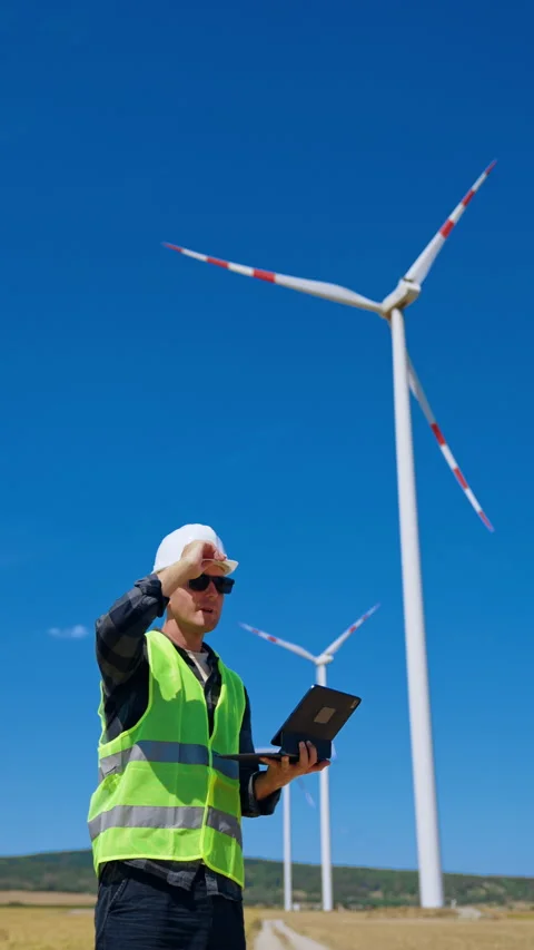 Worker checks data at wind farm under clear blue sky. A man in a hard hat and Stock Footage 342737904
