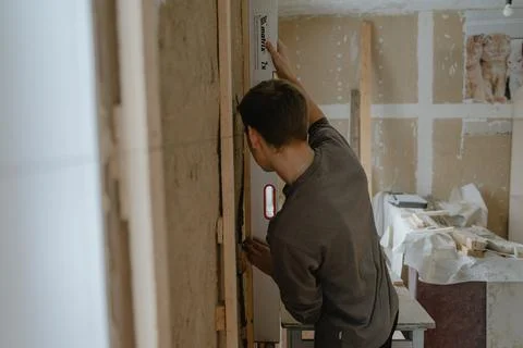 A worker checks the evenness of the walls with a tool, repairing a room, inte Stock Photos