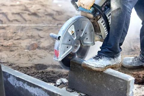 A worker with a circular saw cuts a curb stone close-up. Stock Photos