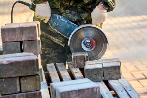 A worker with a circular saw cuts paving slabs in close-up. Stock Photos