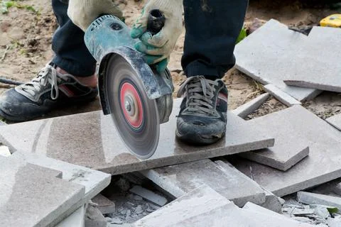 A worker with a circular saw cuts a tile in close-up. Stock Photos