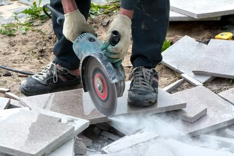 A worker with a circular saw cuts a tile in close-up. Stock Photos