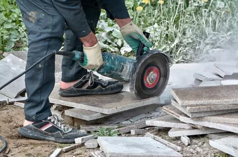 A worker with a circular saw cuts a tile in close-up. Stock Photos