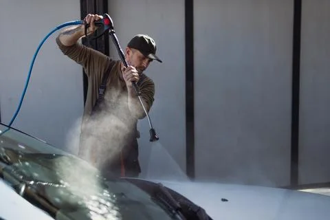 Worker cleaning a dirty car windshield with a high-pressure washer, washing.. Stock Photos