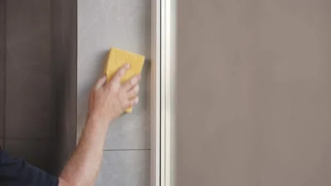 Worker cleaning fresh grout from new ceramic tiles with a sponge during Stock Footage 345753578