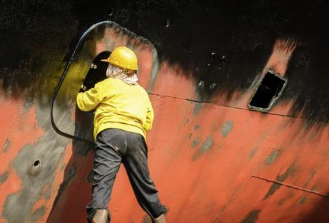 Worker cleaning side of ship at shipyard Stock Photos