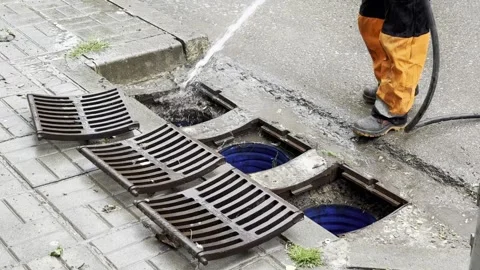 Worker cleans drainage system with high-pressure water hose in urban area Stock Footage 335812400