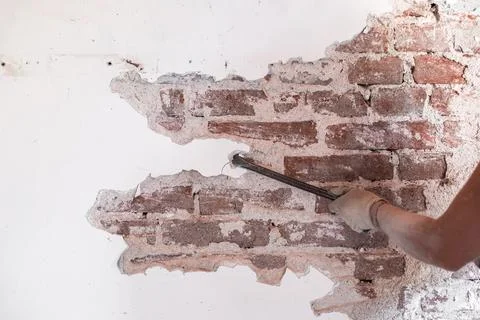 A worker cleans an old brick wall with peeling plaster. Renovation of an ol.. Фото