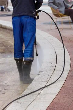 Worker cleans sidewalk with high-pressure water hose Stock Photos
