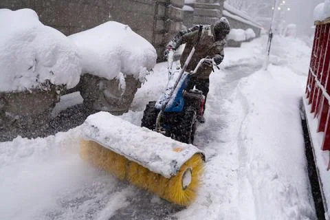Worker clearing sidewalk with snow blower in heavy snowfall Stock Photos