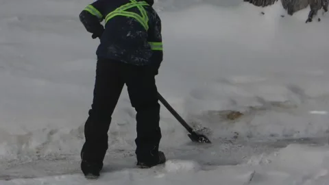A worker clears ice from a sidewalk with a scraper 動画素材 326339471