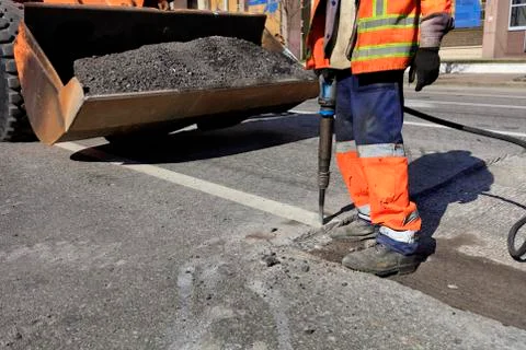 A worker clears a piece of asphalt with a pneumatic jackhammer in road constr Stock Photos