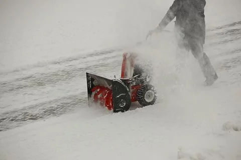 Worker clears snow from the sidewalk with a manual snowplow driven by a gasoline Stock-Fotos