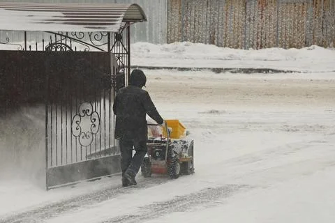 Worker clears snow from the sidewalk with a manual snowplow driven by a gasoline Stock Photos