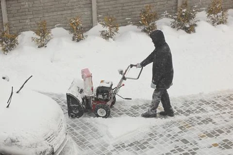 Worker clears snow from the sidewalk with a manual snowplow driven by a gasoline Stock Photos