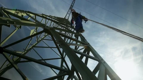 Worker climbing a high-voltage electricity pylon against a clear sky, Video stock 265572283