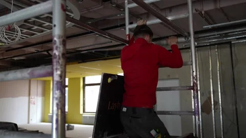 Worker climbing scaffolding at interior construction site. Secure access to Stock Footage 334265156