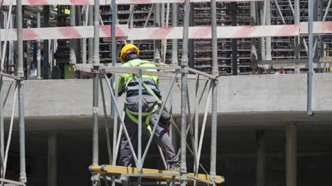 Worker climbs on scaffolding at construction site in bright weather with safety Stock Footage 338245559