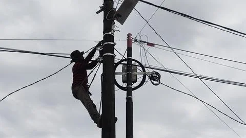 A worker climbs a utility pole, managing electrical wires against a cloudy sk Stock Photos