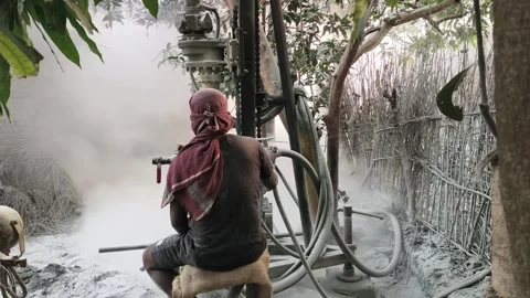 A worker with a cloth head covering operates a borewell drilling rig outdoors. Stock Footage 336710622