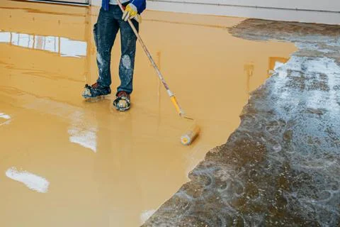 Worker, coating floor with self-leveling epoxy resin in industrial workshop. Stock Photos