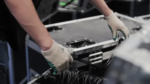 Worker coiling cables above transport case Stock Footage 308624698