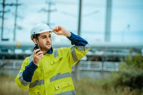 Worker communicates on a radio while wearing safety gear near a constructio.. Stock Photos