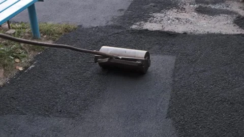 Worker compacting fresh black asphalt edge with a manual metal hand roller 動画素材 339801882