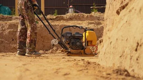 Worker compacting sand and soil with vibratory plate compactor Stock Photos