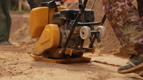 Worker compacting sand foundation using a plate compactor Stock Photos