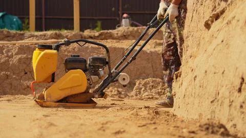 Worker compacting soil with a plate compactor for foundation work Stock Photos