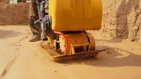 Worker compacting soil with a vibratory plate compactor Stock Photos