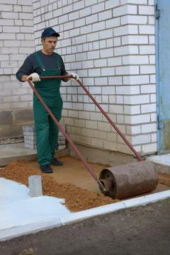Worker compacts soil with a hand roller before construction of  sidewalk Stock Photos