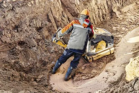 A worker compacts soil or sand with a vibrating plate in a trench at a constr Stock-Fotos