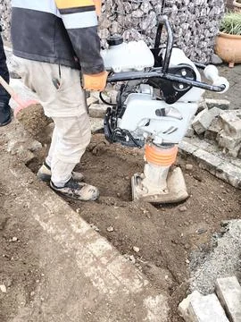 A worker compacts the soil with a vibrating plate 스톡 사진