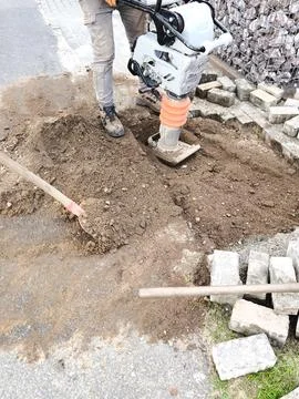 A worker compacts the soil with a vibrating plate Stock Photos