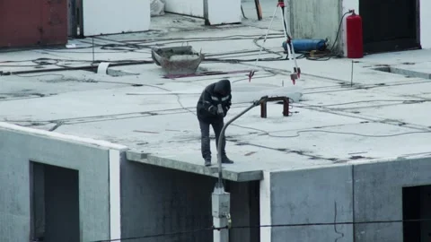 Worker on concrete rooftop of building clearing debris with shovel, construction Stock Footage 325698753