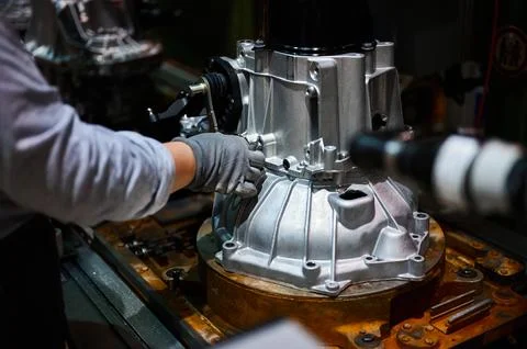 Worker connects car engine gearbox details on shop conveyor Stock Photos