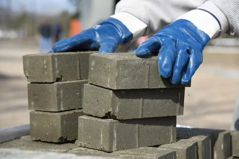 A worker in construction gloves puts paving slabs on a pallet. Stock Photos