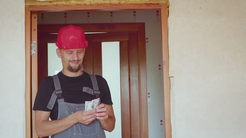 The worker in a construction helmet counts money dollars against the background Stock Footage 94013628