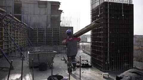 A worker at a construction site carries a beam Stock Footage 232204425