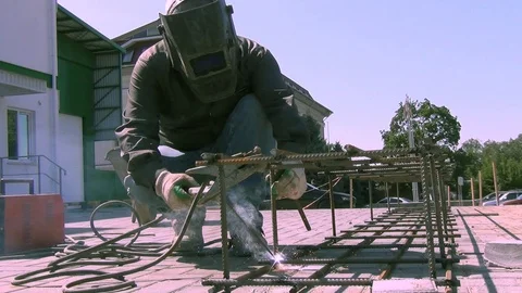 A worker at a construction site conducts welding work on a summer day; close-up  Vidéo 112980608