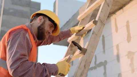 A worker on a construction site hammering nails on a ladder Stock Footage 303230417