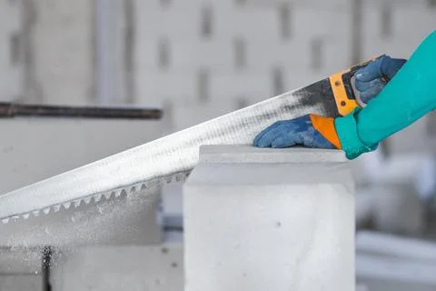 A worker at a construction site saws a building block from aerated concrete at a Fotos de archivo