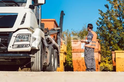 Worker on construction site unloading container for waste from truck Stock Photos