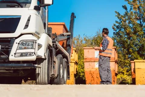 Worker on construction site unloading container for waste from truck Stock Photos