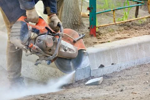 Worker at a construction site using a concrete saw cuts concrete curbs. Stock Photos