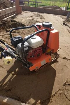 The worker controls the vibrating plate at the construction site, heavy manua Stock Photos